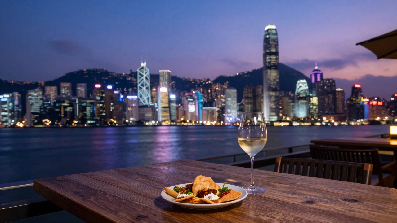 A glass of white wine and snacks on a rooftop table overlooking the illuminated Hong Kong skyline